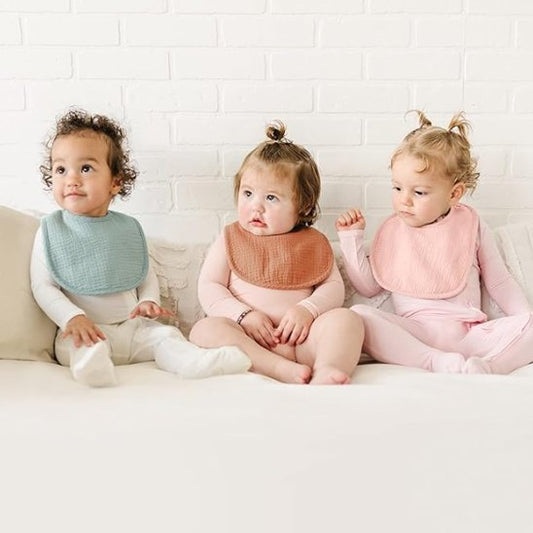 Bavoir, trois bébés assis cote à cote portant chacun un bavoir.  Bavoir bleu, marron et rose poudré